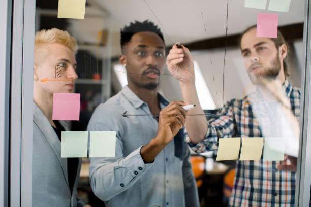 istock Multiethnic creative diverse young business team, colleagues, students, brainstorming on start up, talking, writing ideas on sticky notes, look at glass wall in modern office 1251518857
