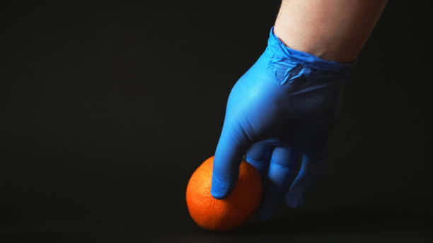 istock A blue gloved hand holds an orange on a black background 1251519164