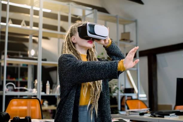 istock Profession and job occupation concept. Young creative woman architect with dreadlocks, testing VR virtual reality glasses, gesturing, touching air to work with new design in creative office studio. 1251519232