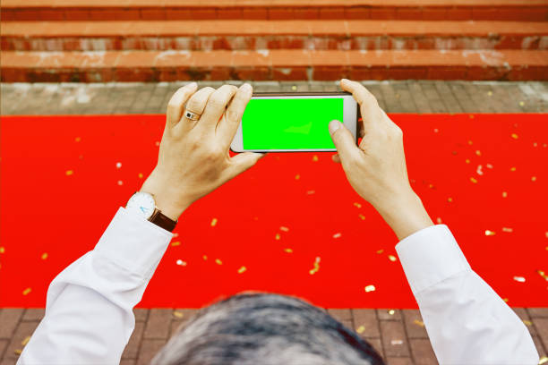 istock Man's hands shooting with phone empty green screen red carpet 1251525093
