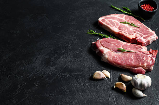 istock Raw pork steak on the bone. Grilled meat. Black background. Top view. Space for text 1251528056