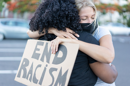 oung african woman hugging a white northern woman after a protest - Northern woman with end racism bannner in her hands - Concept of no racism