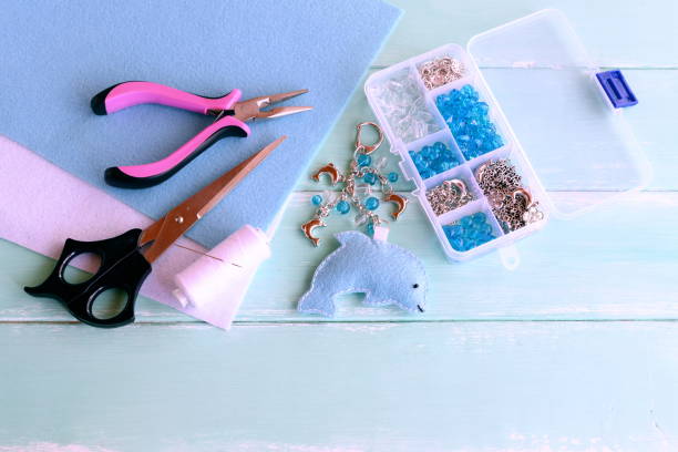 istock Cute felt dolphin with beads. Handmade felt keychain for bag charm. Beads, thread, needle, scissors, pliers. Wooden background. Crafts supplies and tools 1251529842