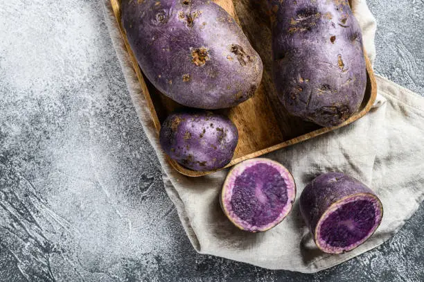 Raw purple potatoes on a chopping Board. Gray background. Top view. Space for text.