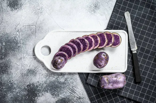 Raw sliced purple potatoes on a white chopping Board. Gray background. Top view. Space for text.