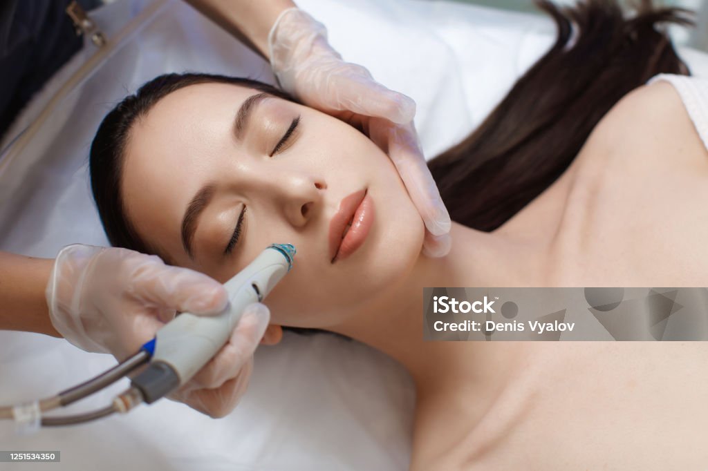 Professional female cosmetologist doing hydrafacial procedure in Cosmetology clinic. Professional female cosmetologist doing hydrafacial procedure in Cosmetology clinic. Doctor use hydra vacuum cleaner. Rejuvenation And Hydratation. Cosmetology Facial Mask - Beauty Product Stock Photo
