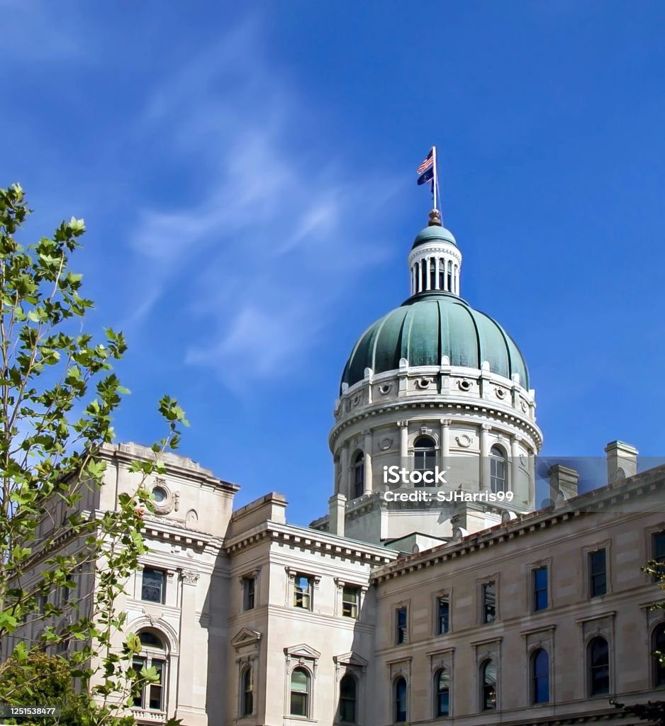 Downtown Indianapolis, Indiana state capital building on a blue sunny day with American flag flying. Indianapolis Capitol Building on a clear blue sky day. Indiana Stock Photo