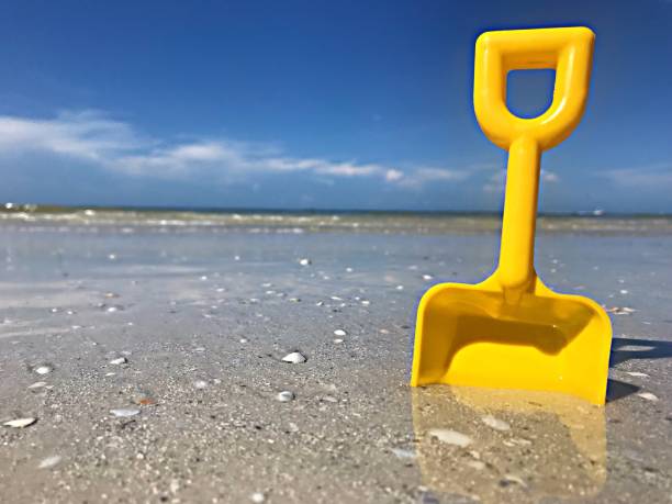 Close up of a small wave washing through a yellow shovel in the sand of a beautiful beach.