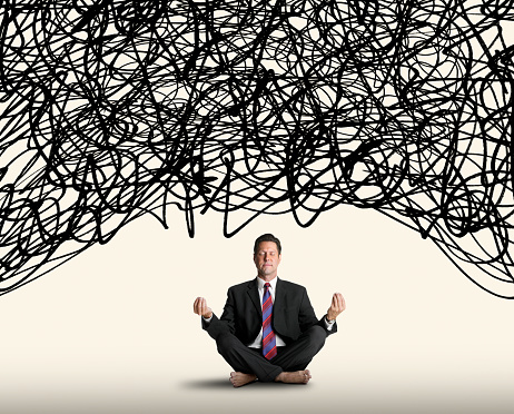 A man sits with his eyes closed and legs folded under him as he strikes a meditative pose as a cloud of randomly scribbled lines that represents stress and chaos hovers above him.