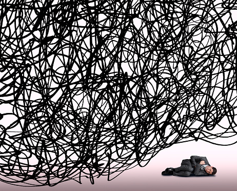 A man under pressure curls up in the fetal position as he lies under a large cloud of randomly scribbled lines that represent huge problems.