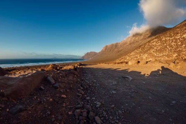 Famara beach with dirty road and mountains in Lanzarote, Canary islands Famara beach with dirty road and mountains in Lanzarote, Canary islands caleta de famara lanzarote stock pictures, royalty-free photos & images