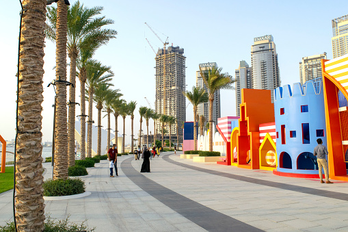 Dubai / UAE - June 19, 2020: Dubai Creek Harbour promenade/walk with beautiful towers, green palms and kids playground. Beautiful view of new modern neighborhood in Dubai.