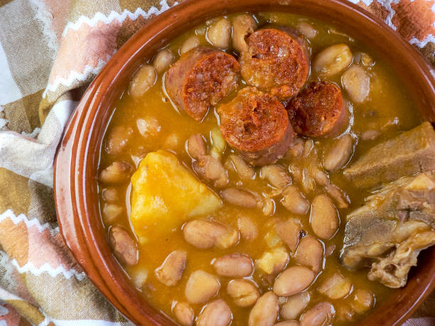 istock Pinto beans with chorizo, potatoes and pork ribs, bread in a brown earthenware container and checkered tablecloth 1251547882