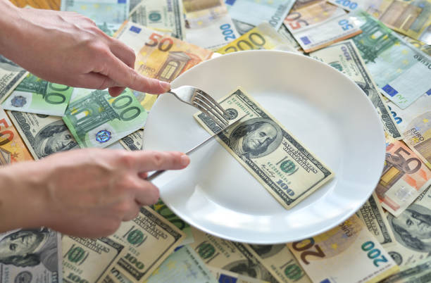 istock Dollar bills lie on a plate. Hand with a fork reaches for dollars 1251548674