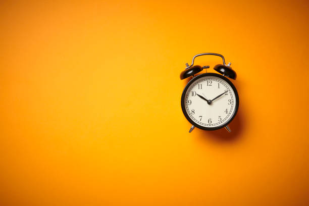 istock Black alarm clock on yellow background. Close up. Top view. 1251550412