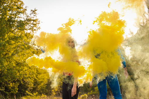 Two girls playing with smoke bombs. There is yellow smoke all around them.