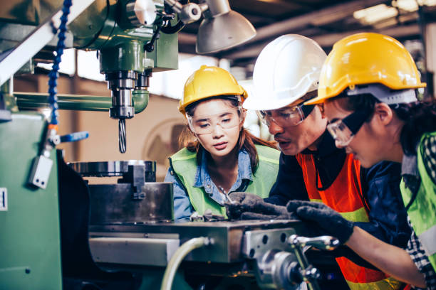 istock Asian male foreman manager showing case study of factory machine to two engineer trainee young woman in protective uniform. teamwork people training and working in industrial manufacturing business 1251551400