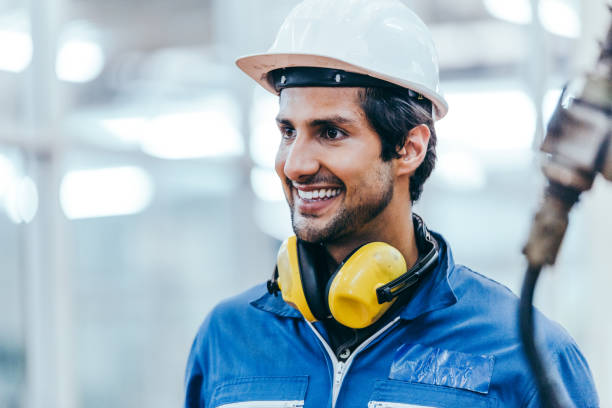 Portrait of smart handsome industrial engineer worker wearing safety helmet and uniform in modern technology industry manufacturing factory. happy positive man back to work from lockdown. copy space Portrait of smart handsome industrial engineer worker wearing safety helmet and uniform in modern technology industry manufacturing factory. happy positive man back to work from lockdown. copy space manufacturing occupation stock pictures, royalty-free photos & images