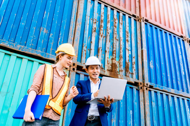 istock Asian male logistic warehouse foreman using laptop checking list of container boxes from cargo freight ship with female assistant. import export shipping business. planning and strategy. copy space 1251551480