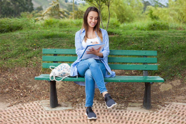 istock Young woman is sitting on a park bench studying with notebook 1251555531