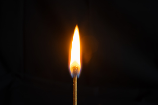Low key, close up burning matchstick on black background with bokeh.