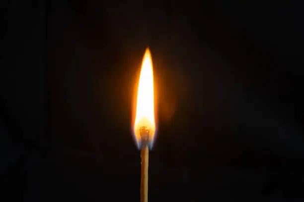 Photo of Low key, close up burning matchstick on black background with bokeh