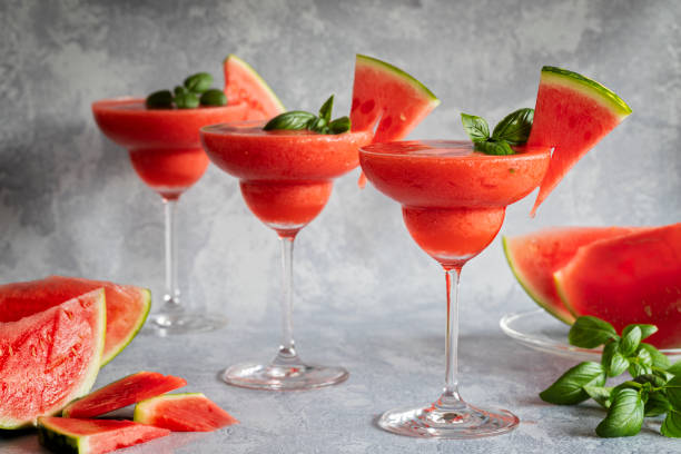 Frozen red drink margarita garnished with watermelon and basil. Three red drinks in a row. Three fresh frozen blended margarita drinks with strawberries and watermelon. The drinks are garnished with basil leaves and watermelon. Gray background. Horizontal with copy space room for text. frozen rose stock pictures, royalty-free photos & images