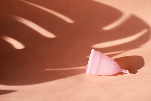 Copa menstrual sobre un fondo rosado con la sombra de una hoja de palma tropical. El concepto de días críticos durante las vacaciones y el verano photo