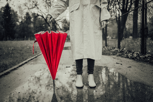 Woman in raincoat with a red umbrella standing in the rain