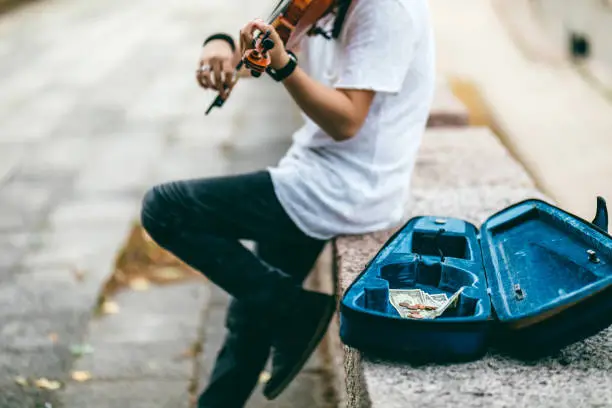Young Caucasian man playing violin outdoor for money.