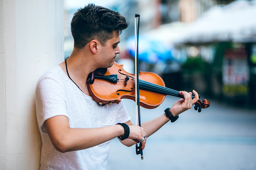 Young Caucasian man playing violin on a city street for money.