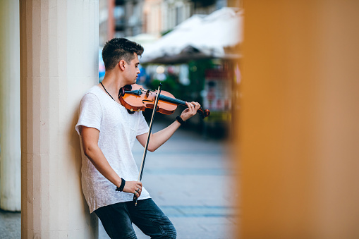 Young Caucasian man playing violin on a city street for money.