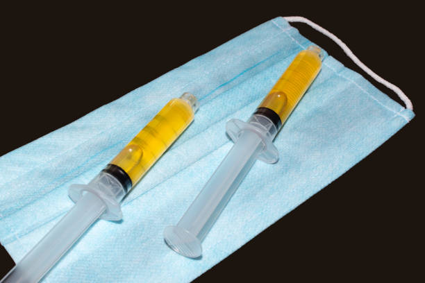Syringes with blood plasma on a medical protective mask. Blood plasma as coronavirus treatment solution. Syringes with blood plasma on a medical protective mask. Blood plasma as coronavirus treatment solution. Platelet-Rich plasma preparation for plasmolifting therapy. Isolated on a dark background. environmental regeneration photos stock pictures, royalty-free photos & images