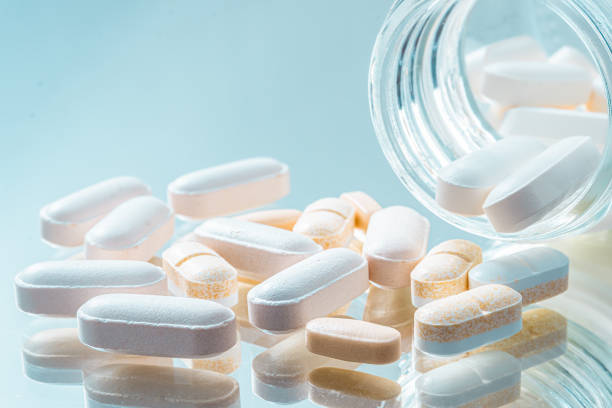 White and yellow tablets or pills or medication or drugs with bo White and yellow tablets or pills or medication or drugs with bottle closeup. Selective focus. Pharmacy, medicine, medical treatment concept. drug manufacturing stock pictures, royalty-free photos & images