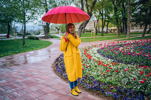Young smiling woman walking through the park in the rain, holding red umbrella