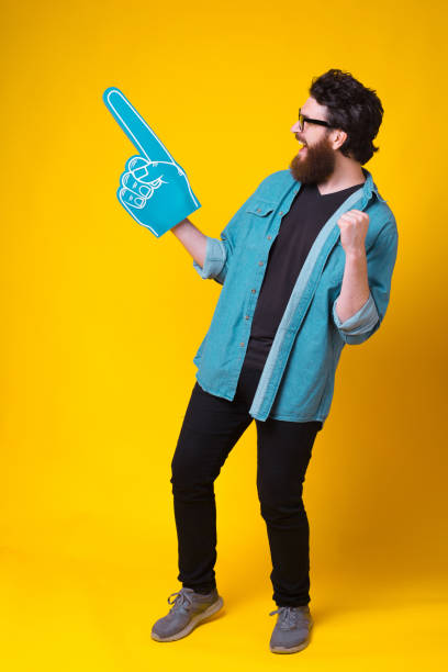 el hombre barbudo está gritando sí mientras usa el guante azul de la espuma del ventilador - hip expressing positivity full blue fotografías e imágenes de stock