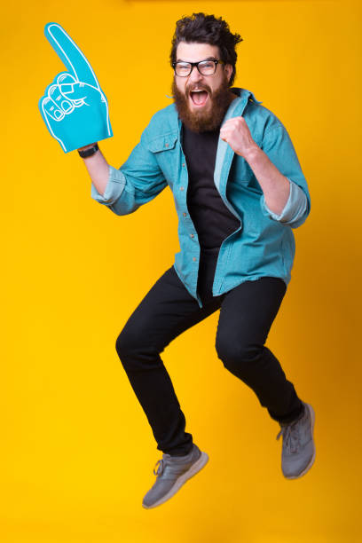 Excited berded man wearing a fan foam glove while jumping.