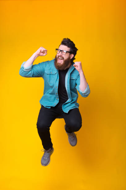 istock Happy bearded hipster is jumping in a studio making winner gesture while screaming 1251573654