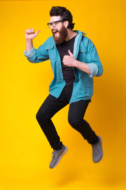 istock Singing or screaming bearded man is jumping over yellow background 1251573655