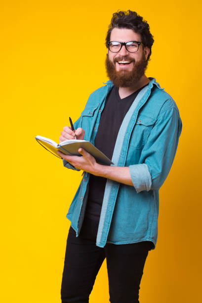 istock Cheerful man is writing in his journal over yellow background. 1251573662