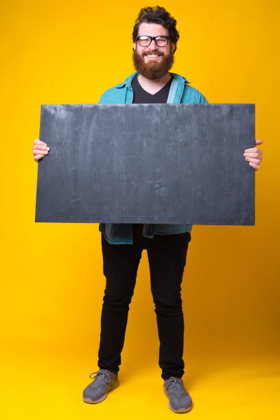 カメラのひげを生やしたヒップスターに微笑むきれいな黒いボードを保持しています - black sign holding vertical ストックフォトと画像