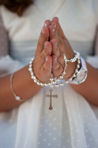 hands of a girl praying with a rosary dressed in communion