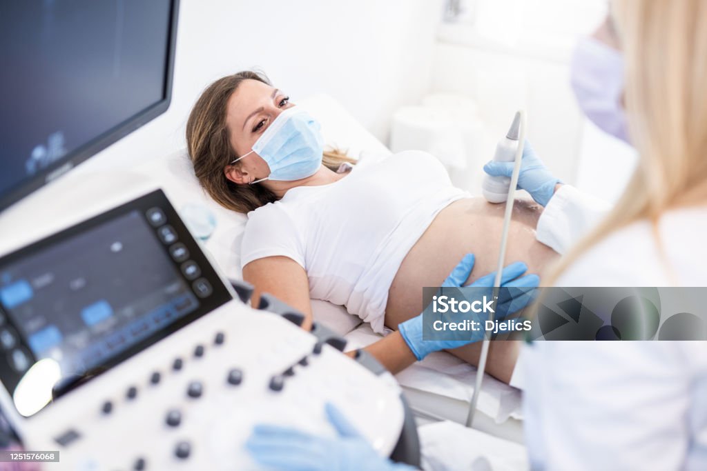 Pregnant woman on ultrasound. Ultrasound pregnancy examination of young woman in a Medical Clinic during Covid 19 outbreak. Pregnant Stock Photo