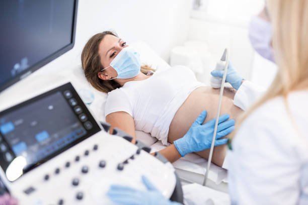 Pregnant woman on ultrasound. Ultrasound pregnancy examination of young woman in a Medical Clinic during Covid 19 outbreak. pregnant ultrasound stock pictures, royalty-free photos & images