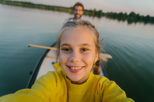 Selfie of girl in yellow sweater canoeing on lake with brother  at sunset