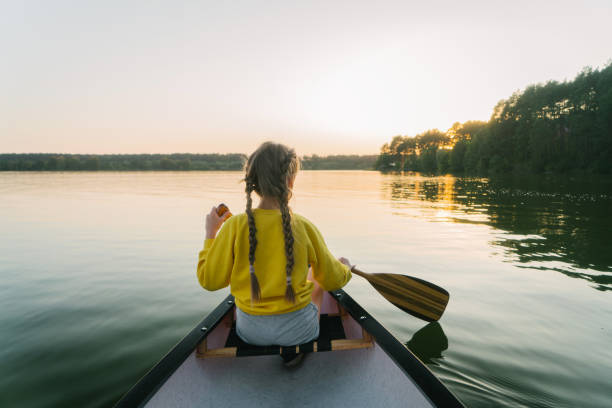 Young Caucasian woman canoeing on lake at sunset