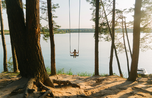 Girl on swing over the lake in summer