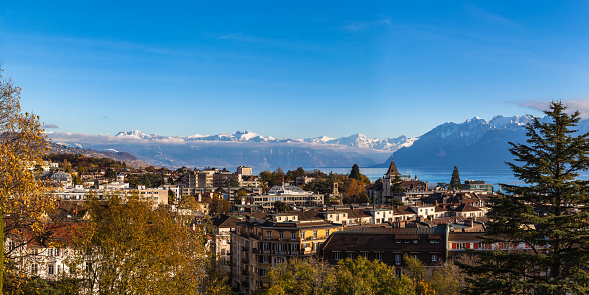 Aerial panorama view of Lausanne cityscape with snow covered French Alps and Lake Geneva (Lake Leman) in background on a sunny autumn day with blue sky cloud, Canton of Vaud, Switzerland