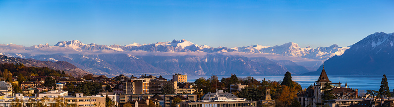 Stunning aerial panorama view of Lausanne cityscape with Lake Geneva (Lake Leman) and snow covered French Alps in background on a sunny autumn day with blue sky cloud, Canton of Vaud, Switzerland