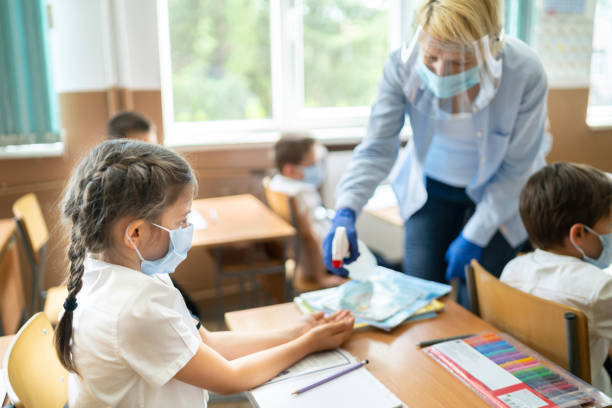 COVID-19. Using hand sanitizer in the classroom Service staff disinfecting hands of a girl in the classroom reopening photos stock pictures, royalty-free photos & images